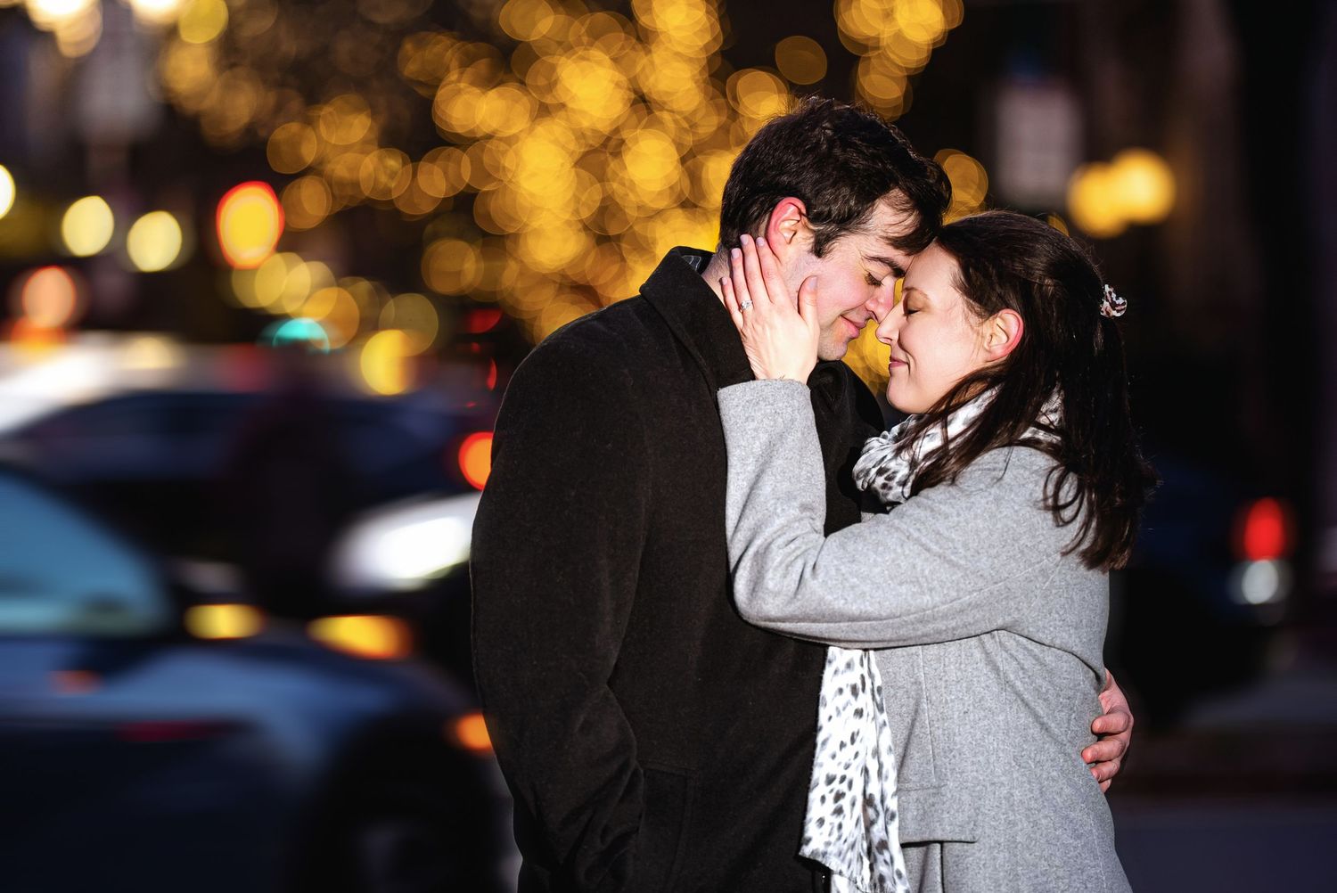 A romantic couple embraces outdoors at night with twinkling bokeh lights in the background.