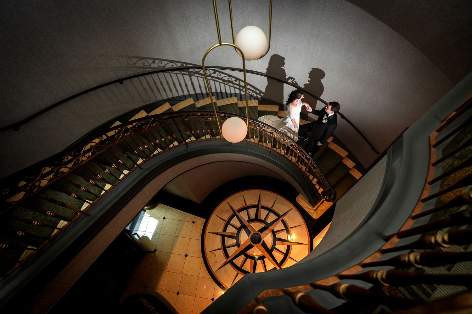 Elegant spiral staircase with ornate iron railings, a couple in wedding attire posing on the steps of a grand historic building.