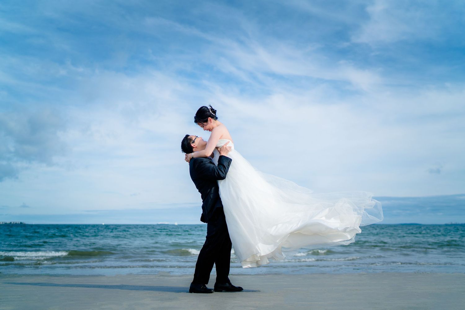 A romantic beach wedding photo with waves and flowing white dress.