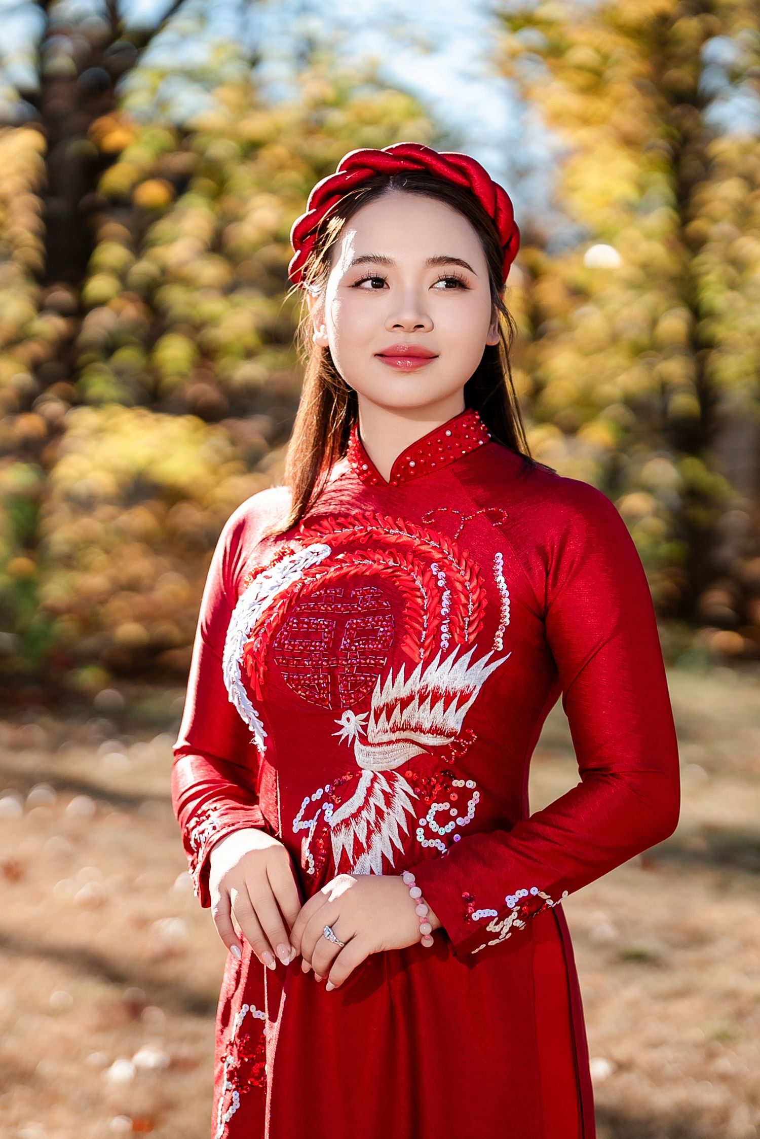 Red traditional dress with dragon embroidery photographed against autumn foliage background.