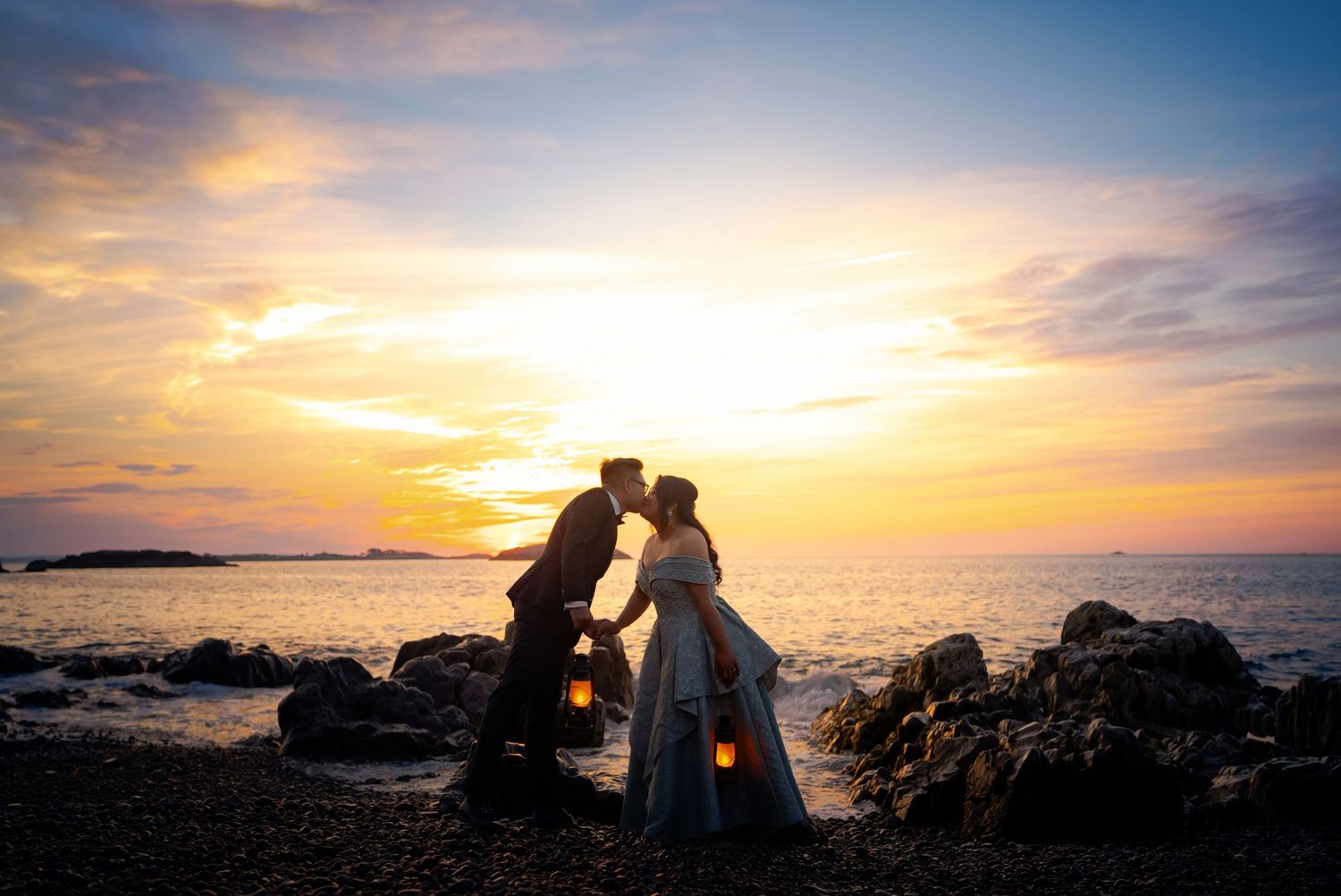 Silhouettes embrace against a vibrant orange and purple sunset over the ocean.