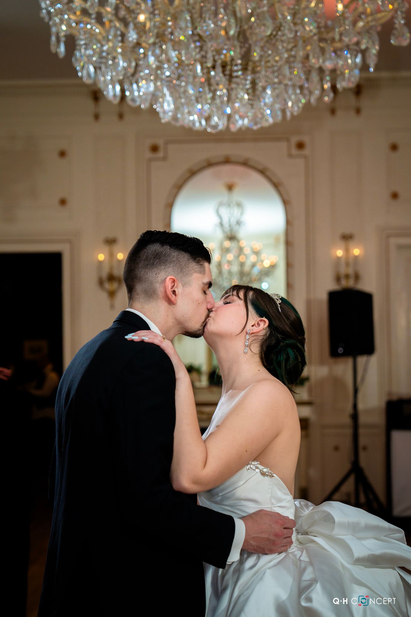 A romantic kiss under an elegant crystal chandelier during a wedding reception.