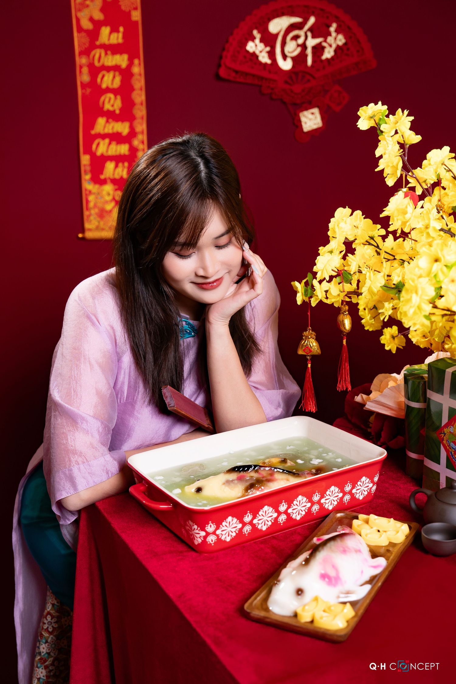 A person in a lilac top looks down at a decorative tray during Lunar New Year celebrations with golden decor.