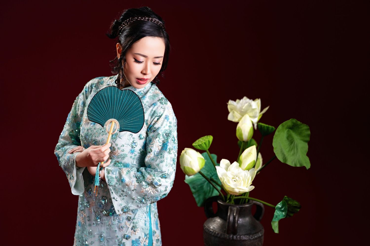 A person in a blue floral kimono stands elegantly with white lotus flowers against a dark background.