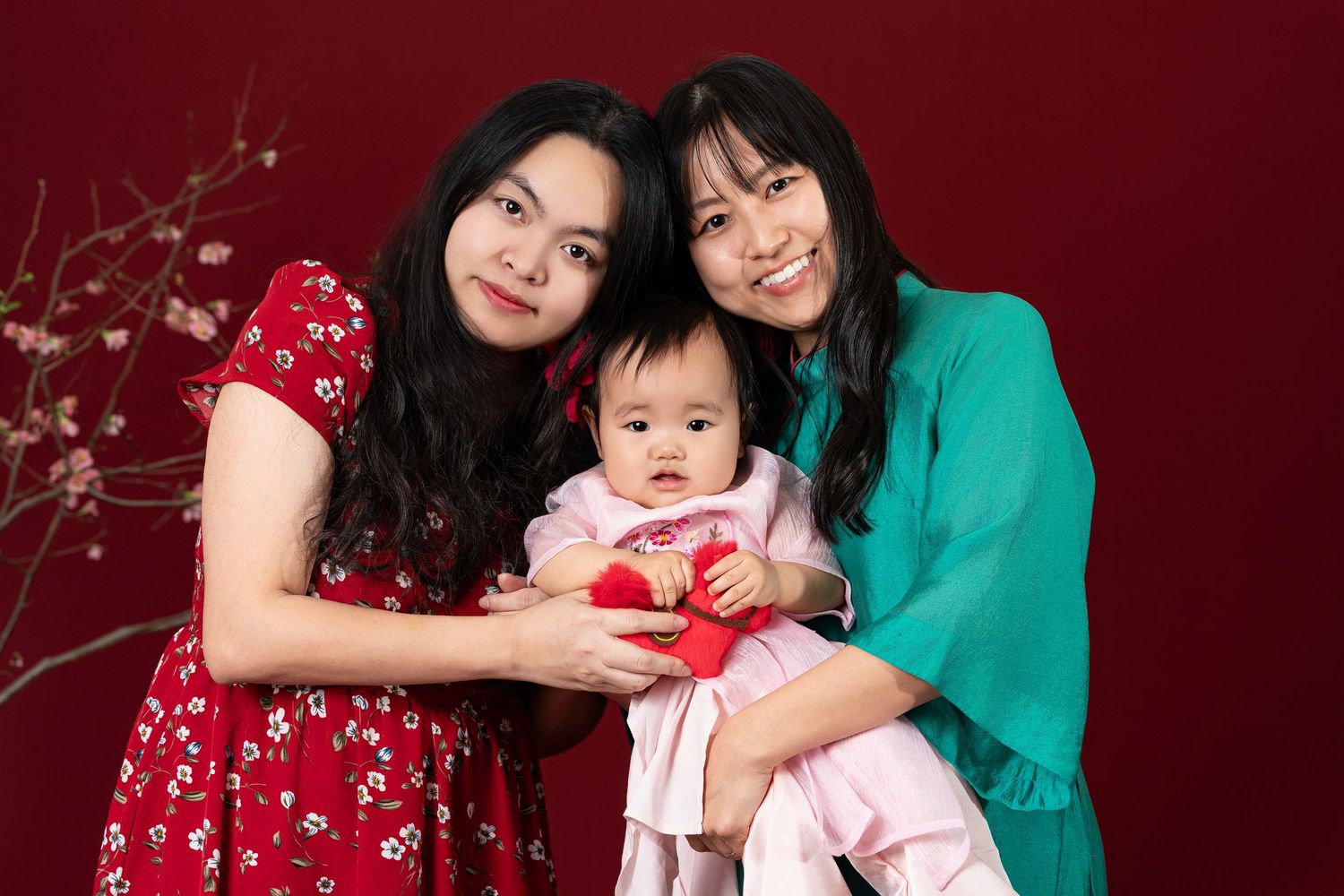 A family poses together in formal attire against a deep red backdrop with decorative cherry blossom branches.