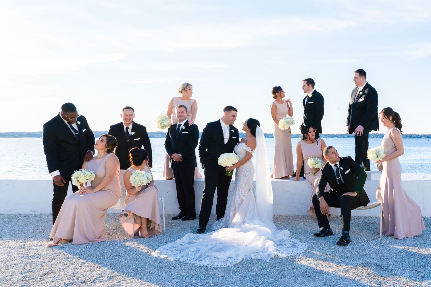 A wedding party poses on a white sandy beach with the ocean in the background creating a scenic beach wedding photo.