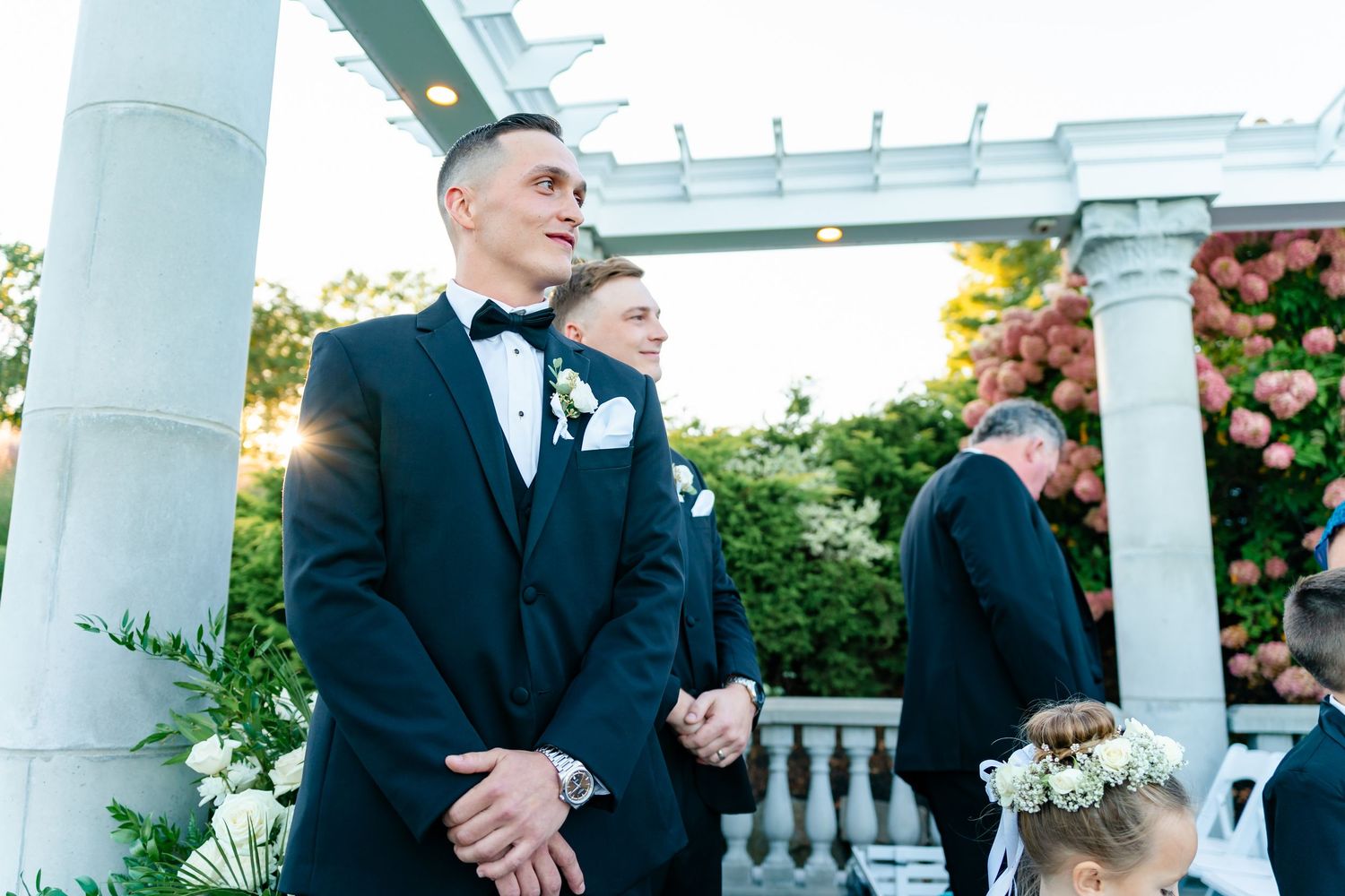 Elegant outdoor wedding venue with white pillars and pergola against a bright sky.