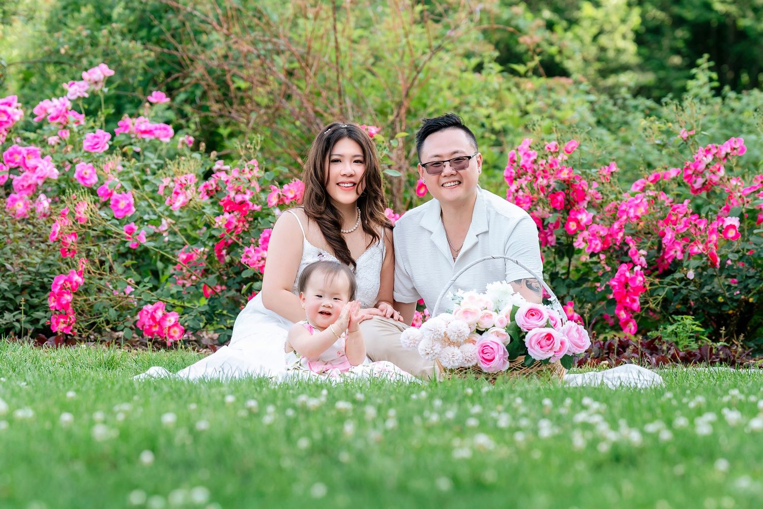 Family portrait session in garden with bright pink roses and green landscaping.