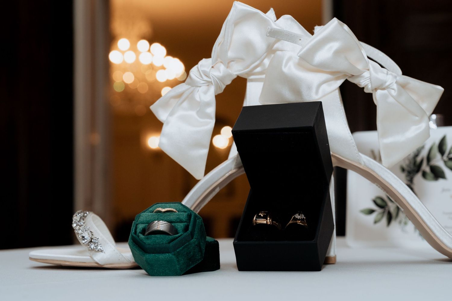 Wedding accessories including white shoes, green clutch purse, and black box arranged on light surface with warm lighting.