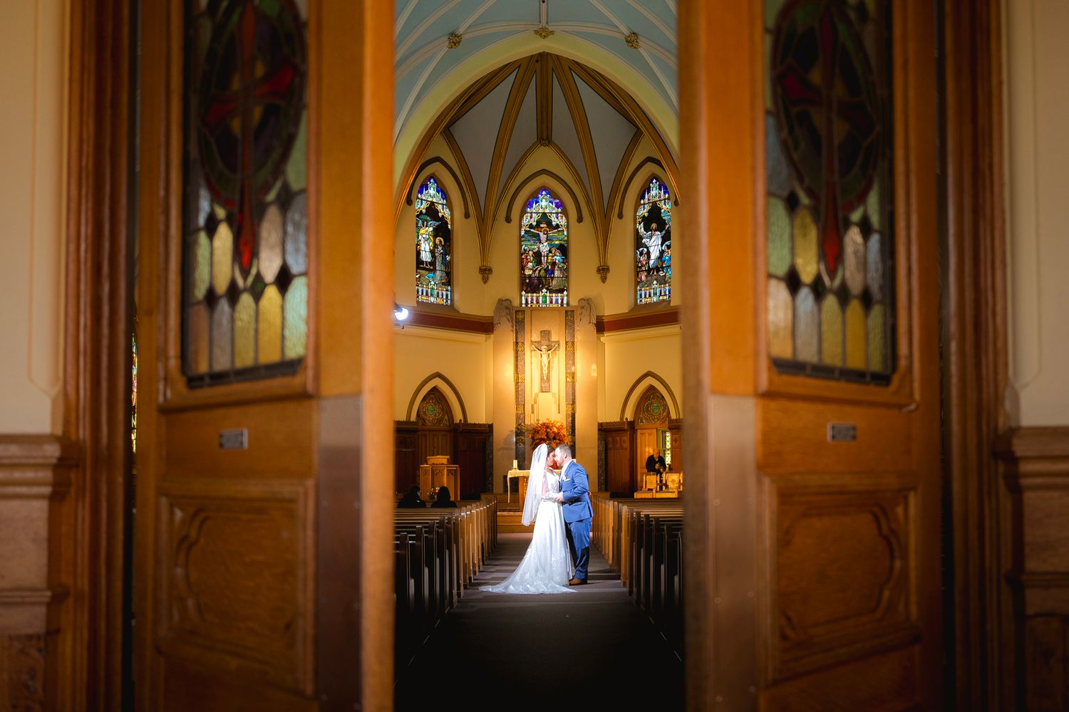 A wedding couple stands silhouetted in a grand cathedral with soaring arches and warm lighting creating a romantic ambiance.