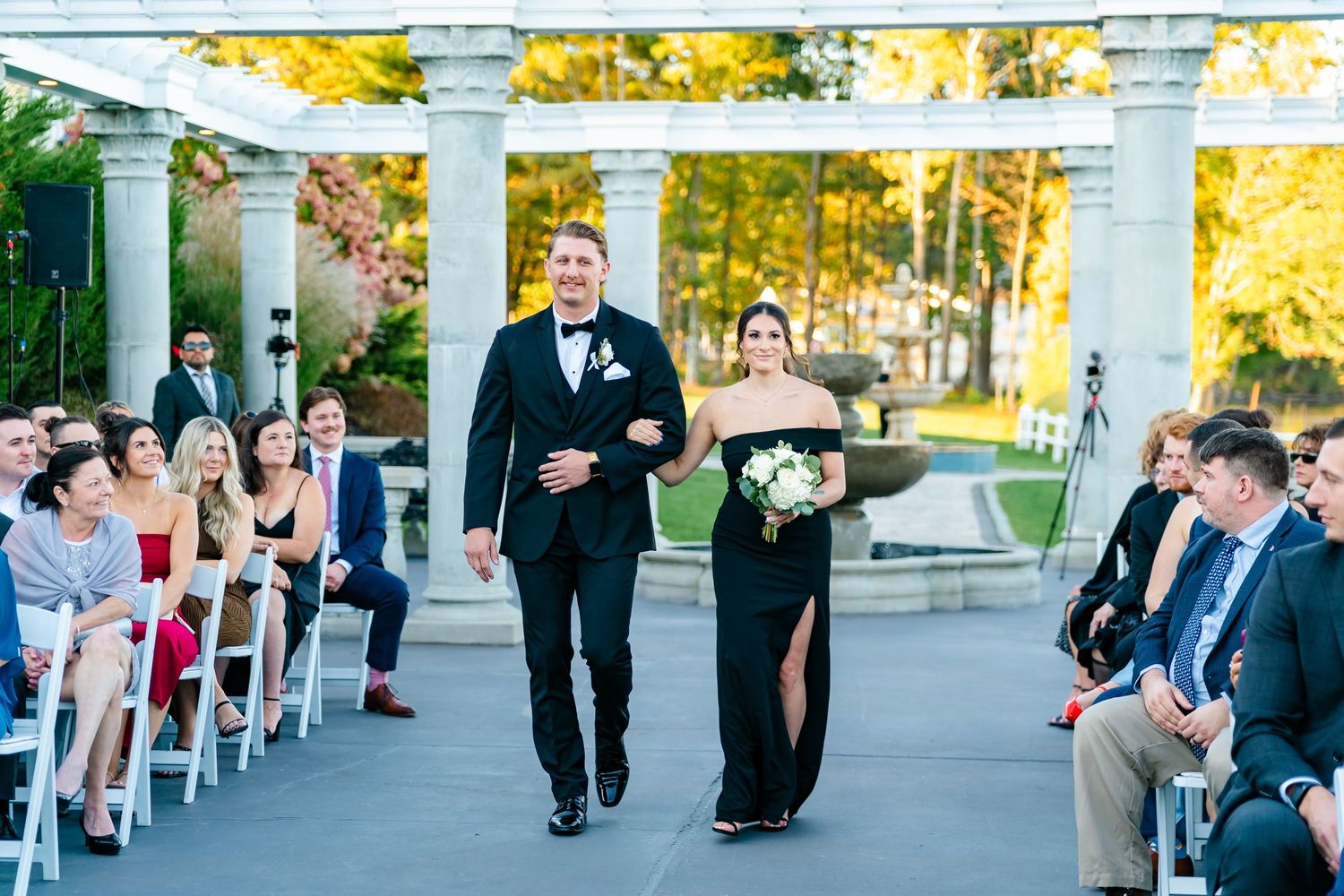 Outdoor wedding ceremony venue with white columns and chairs arranged in rows.