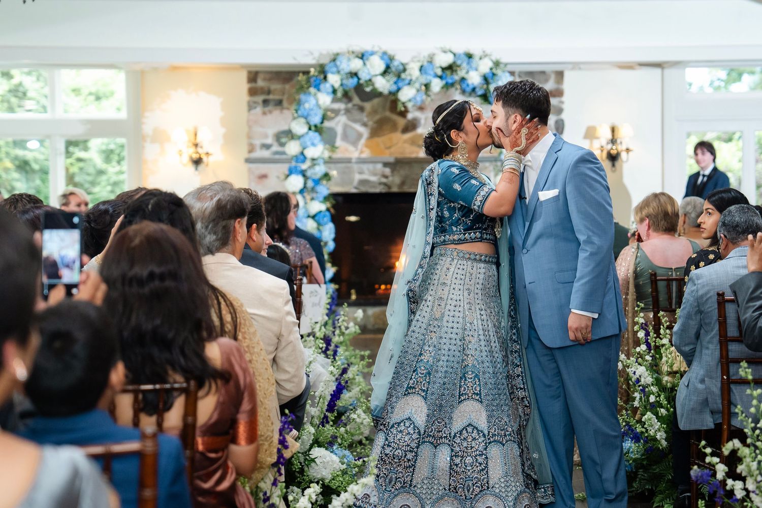 Wedding ceremony moment with couple in front of floral-decorated fireplace.