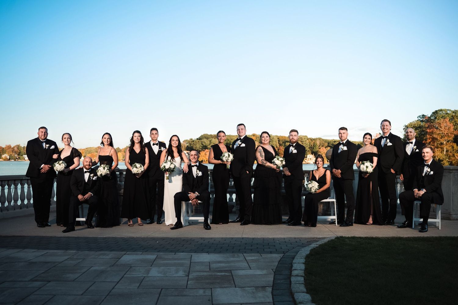 Large wedding party group photo arranged outdoors with formal attire against natural backdrop.