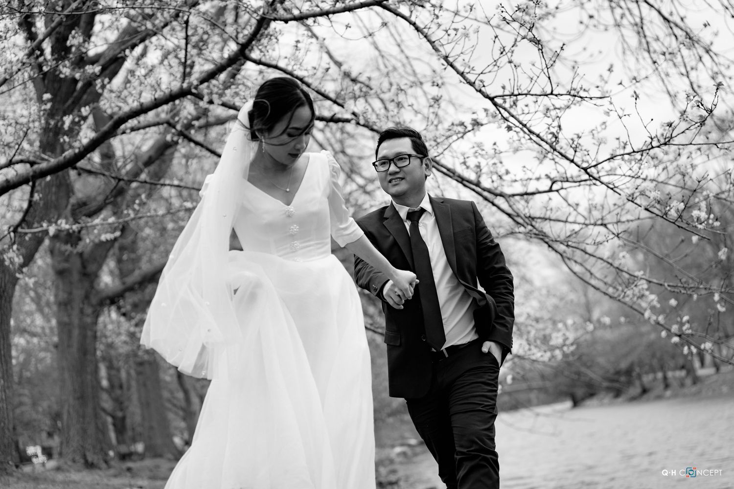 A black and white wedding portrait captured under blooming spring trees.
