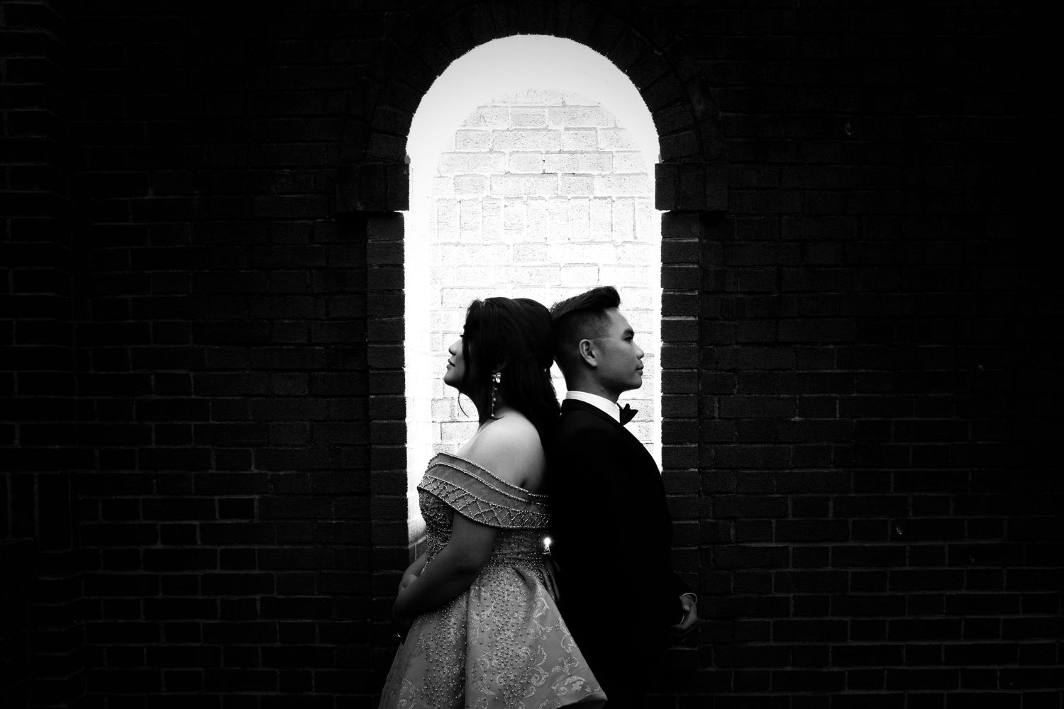 Dramatic black and white portrait with backlit archway creating silhouettes.