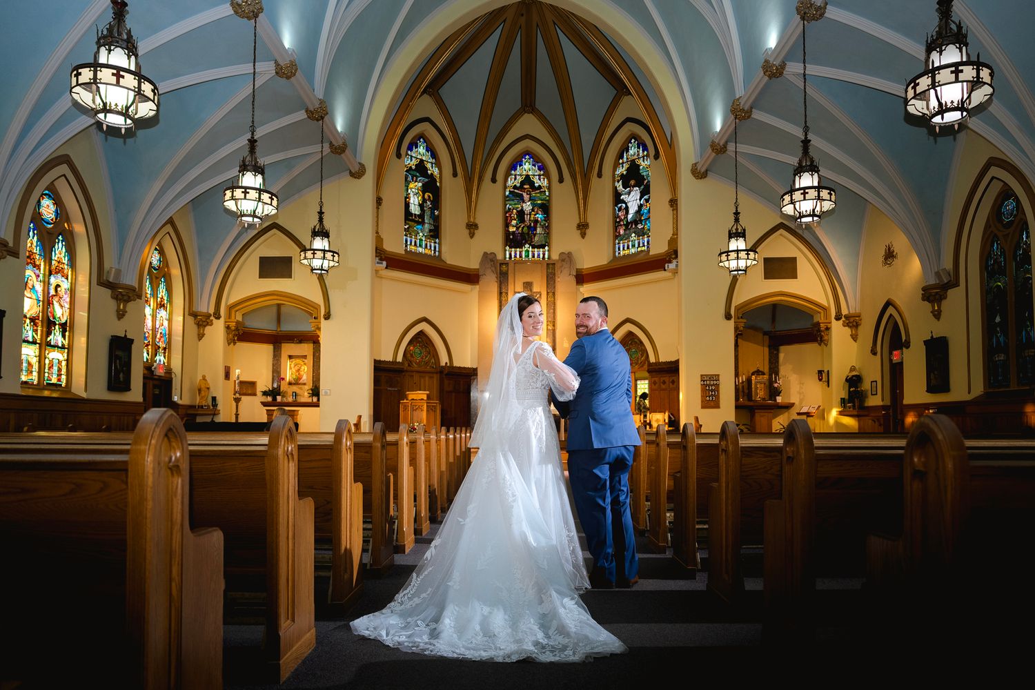 A wedding couple stands in a beautiful Gothic church with vaulted ceilings and stained glass windows.