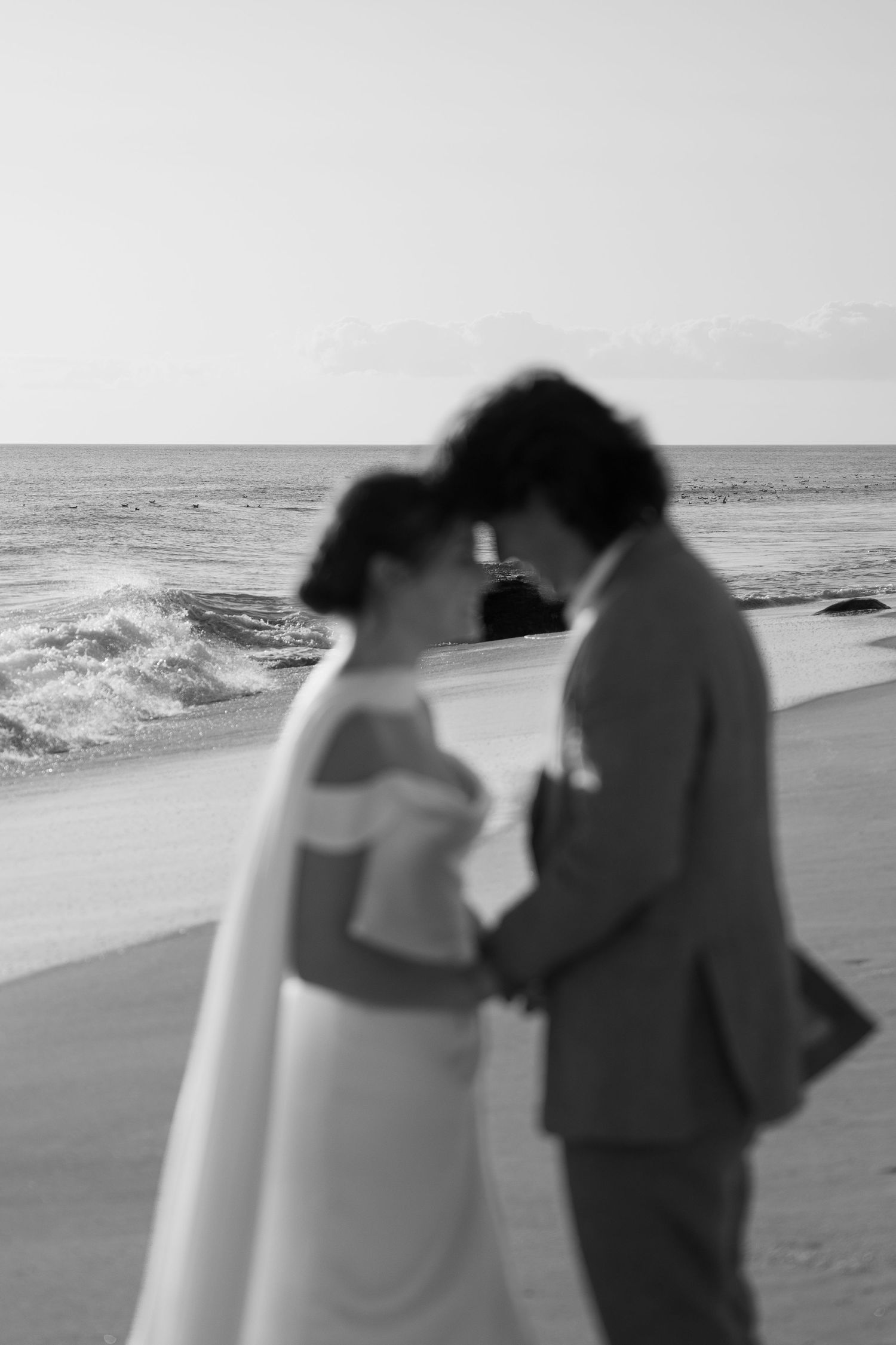 A romantic black and white beach scene with a surfboard silhouetted against crashing waves at sunset.