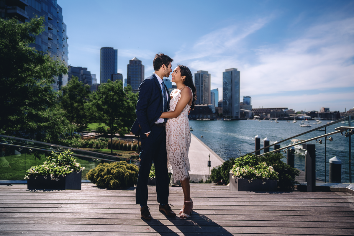 A waterfront engagement session with modern city skyline and harbor views.