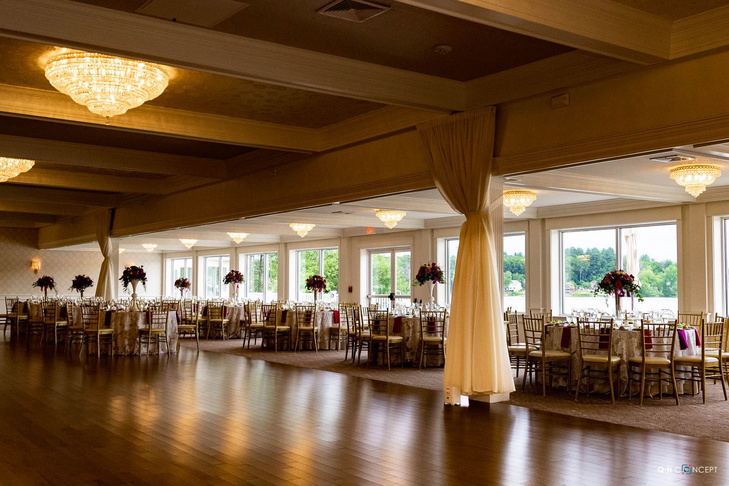 Elegant banquet hall with crystal chandeliers, white drapes and round tables set for a formal event.