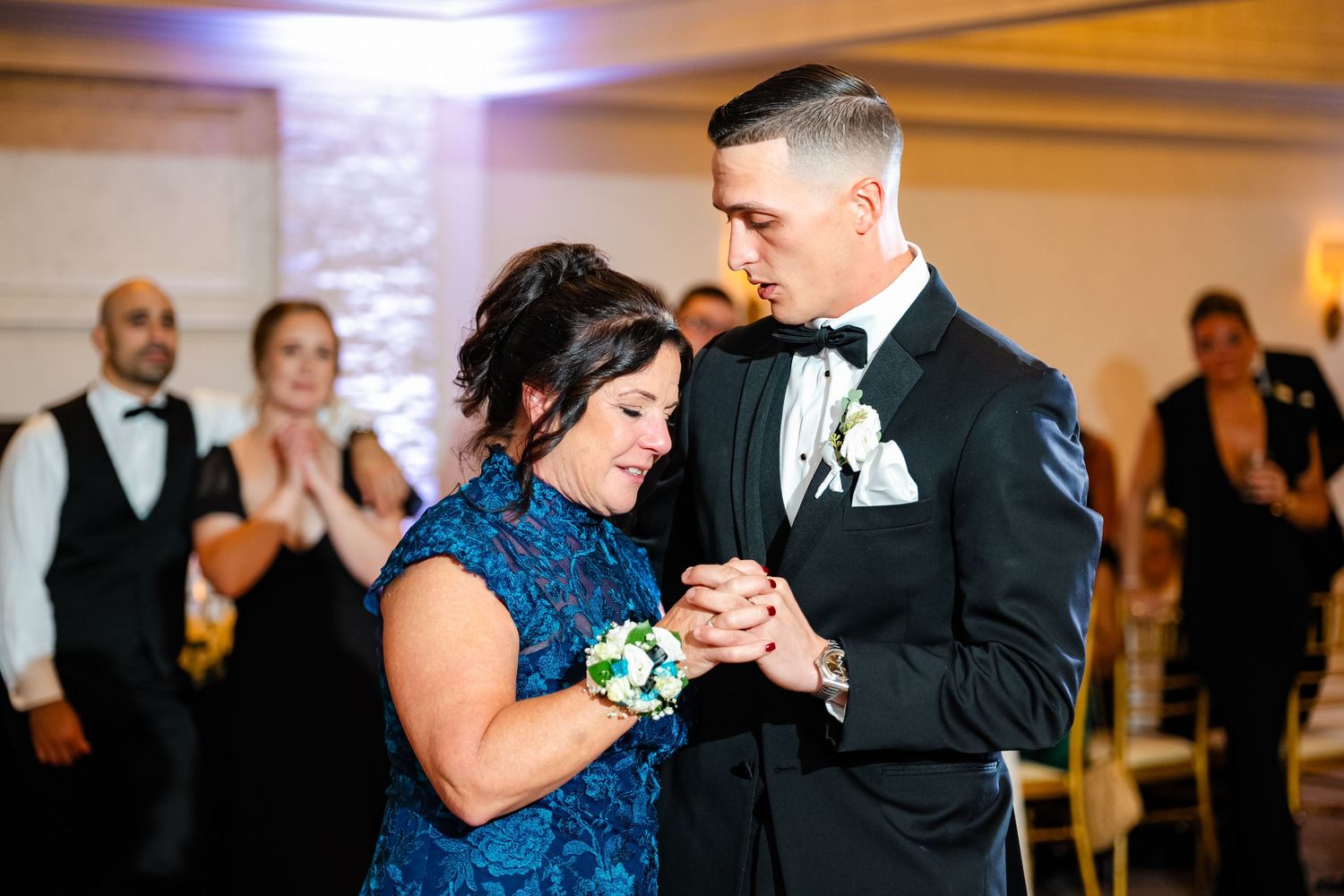 Wedding guests dancing and celebrating at an elegant indoor reception venue with warm lighting.