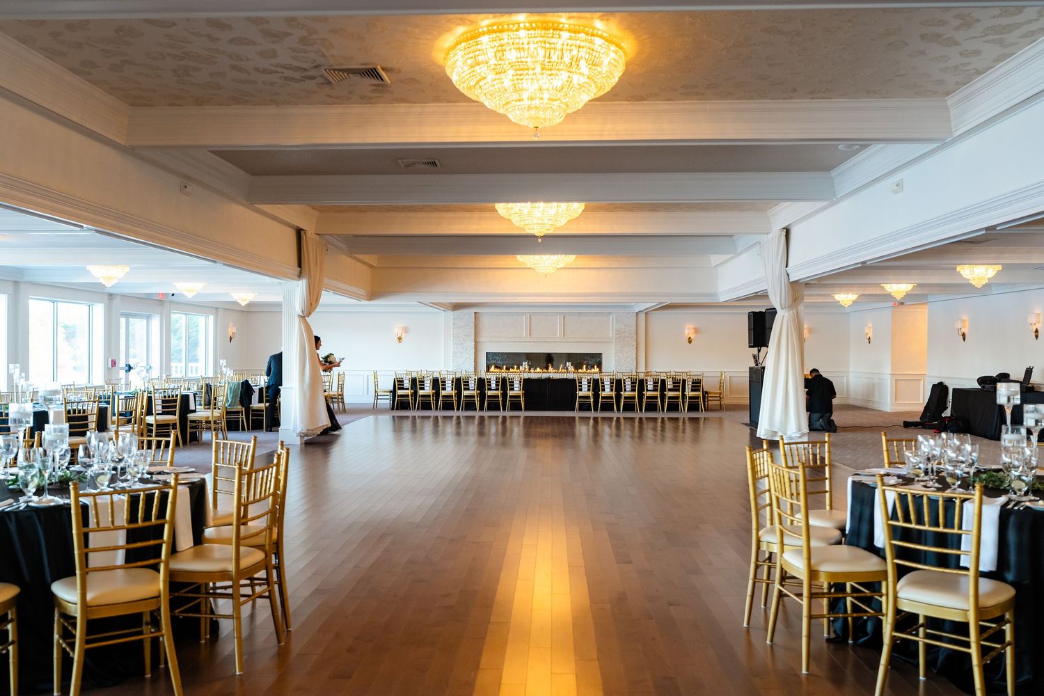 Panoramic view of a modern event space with white walls, chandeliers, and rows of dining tables set for a formal occasion.