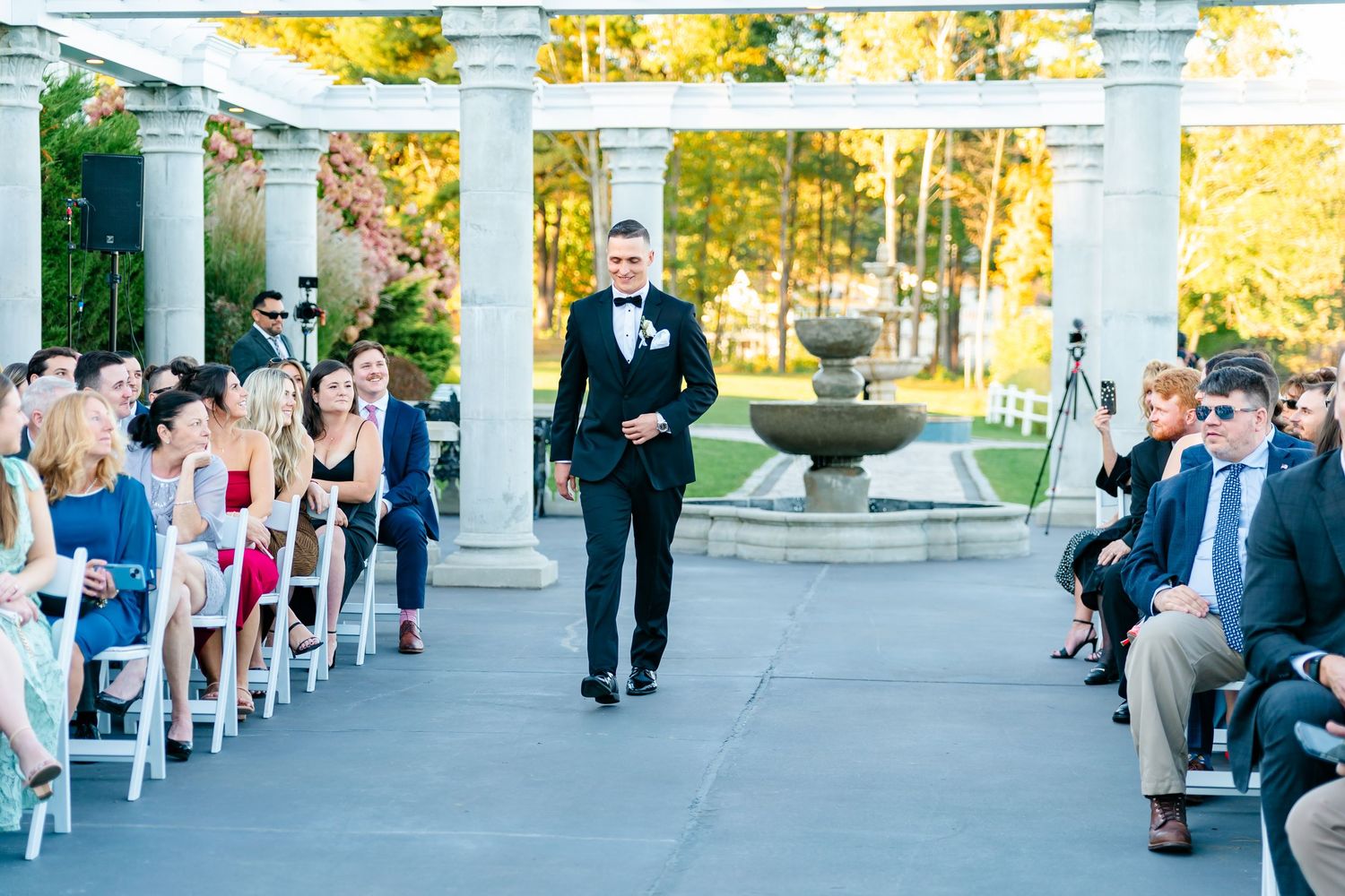 Outdoor wedding ceremony setup with white chairs and pillars along a garden pathway.