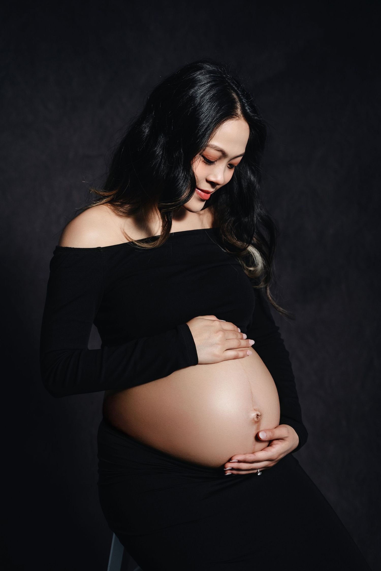Artistic maternity photo series in dark moody lighting showing silhouette of pregnant belly against black background.