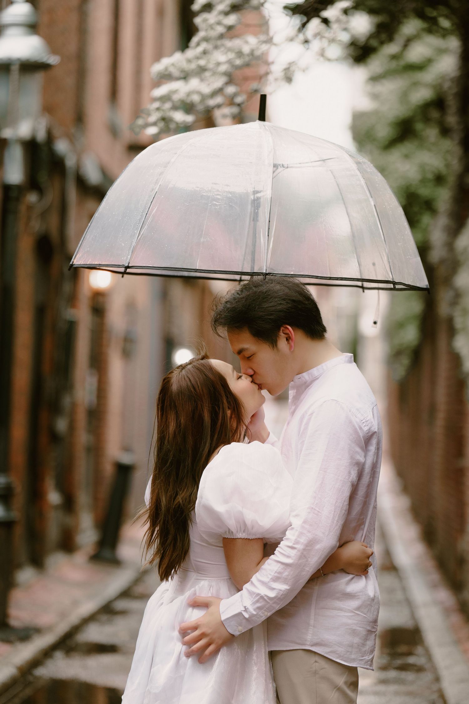Romantic couple sharing intimate moments under clear umbrellas on a rainy city street.