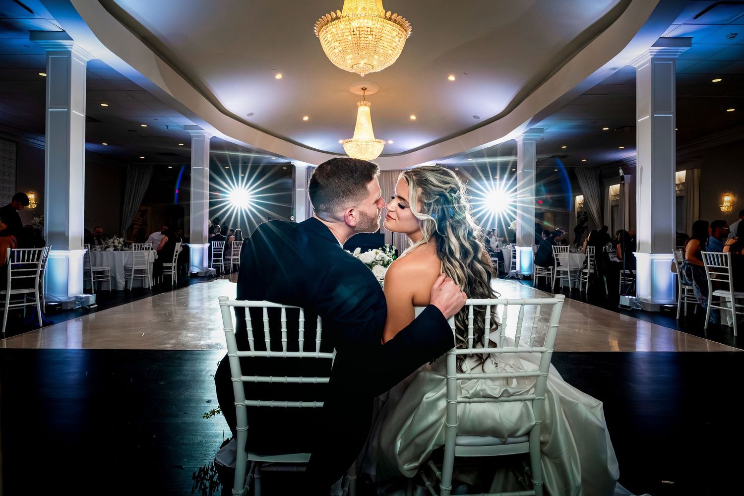 A couple shares an intimate moment on the dance floor under a crystal chandelier at an elegant wedding reception.