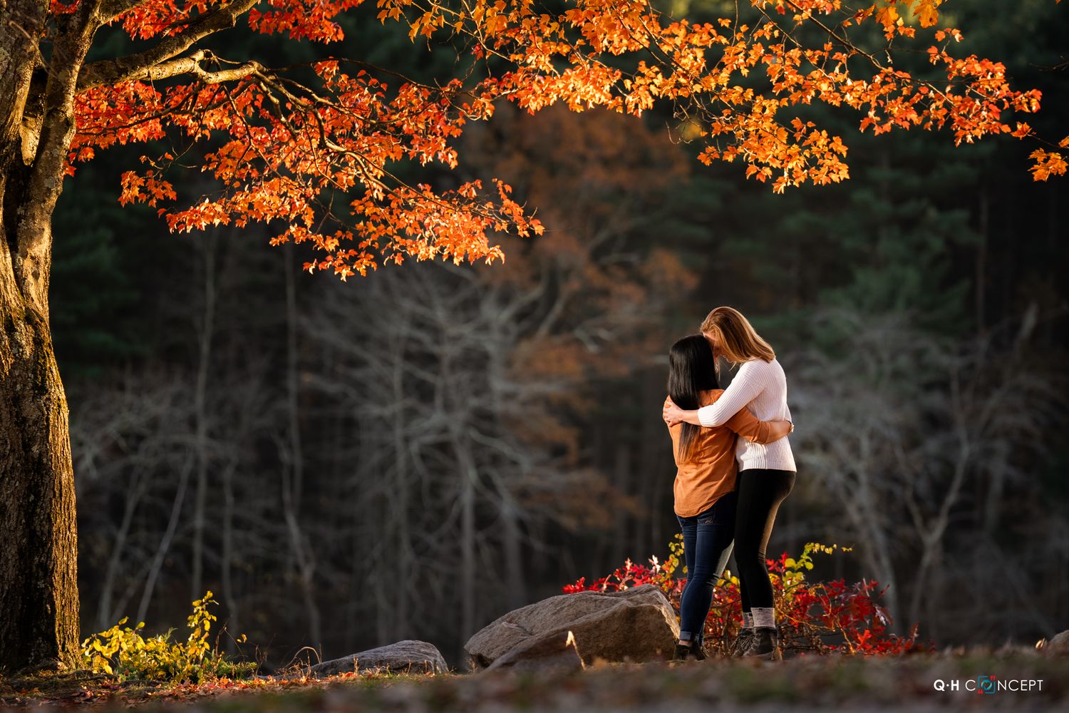 Couple embraces under vibrant orange autumn foliage at sunset in a scenic park setting.