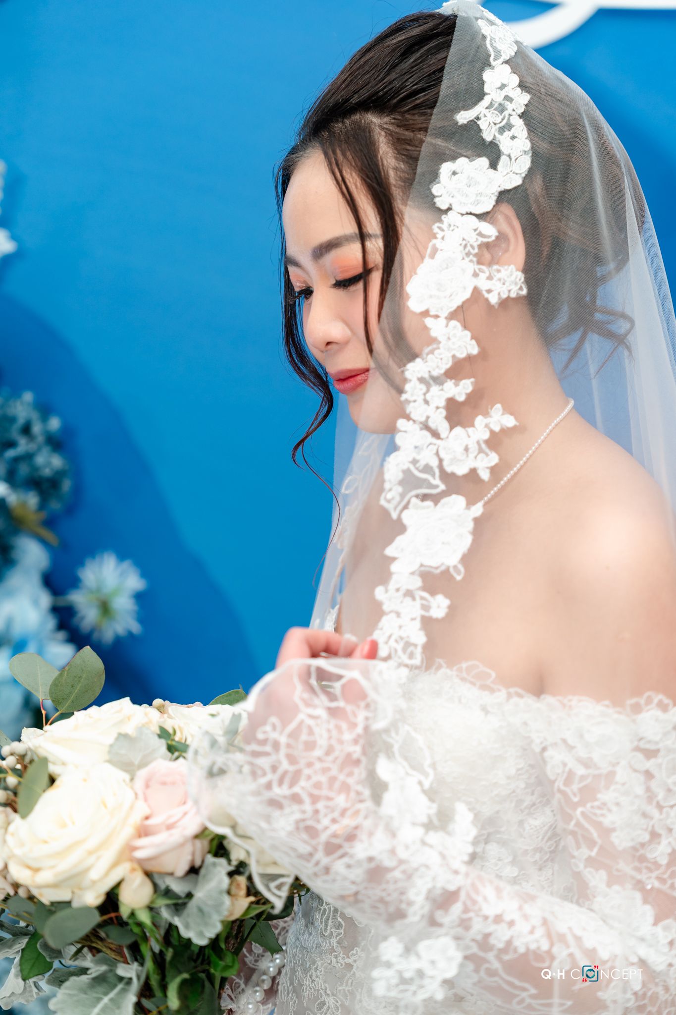 Delicate white lace veil and roses create an elegant bridal portrait against a vibrant blue background.