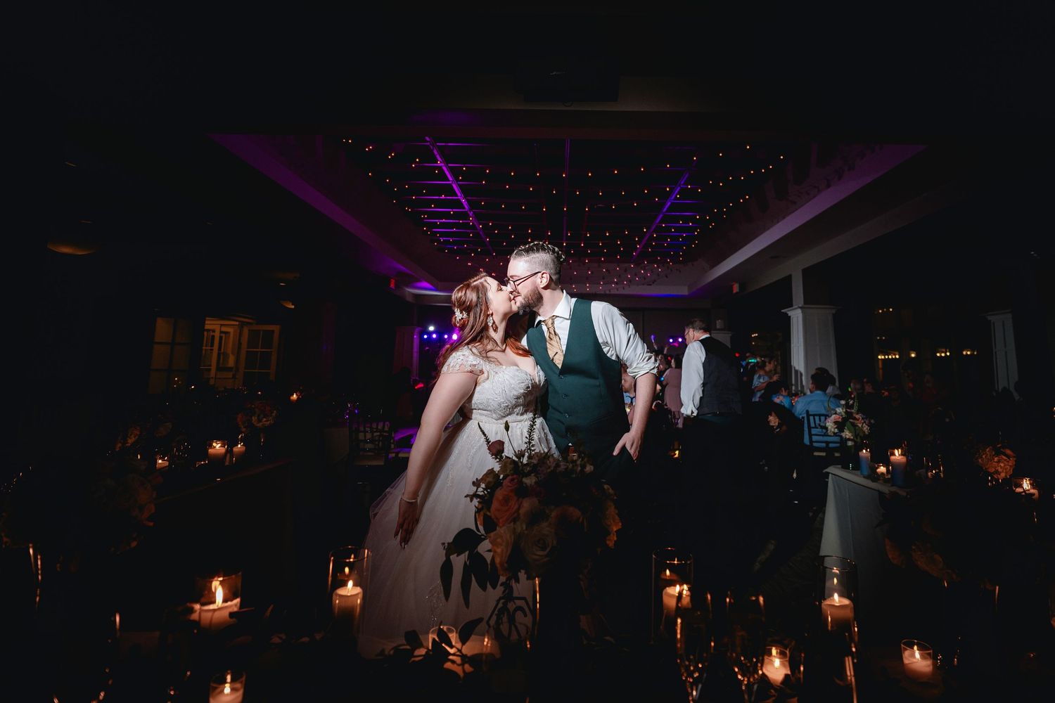 Wedding reception dance floor scene with purple ambient lighting and hanging decorations.