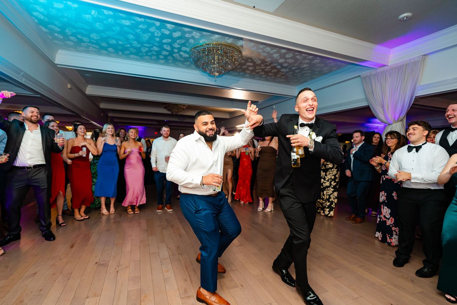 Wedding guests dance and celebrate on a illuminated dance floor with blue ceiling lights.