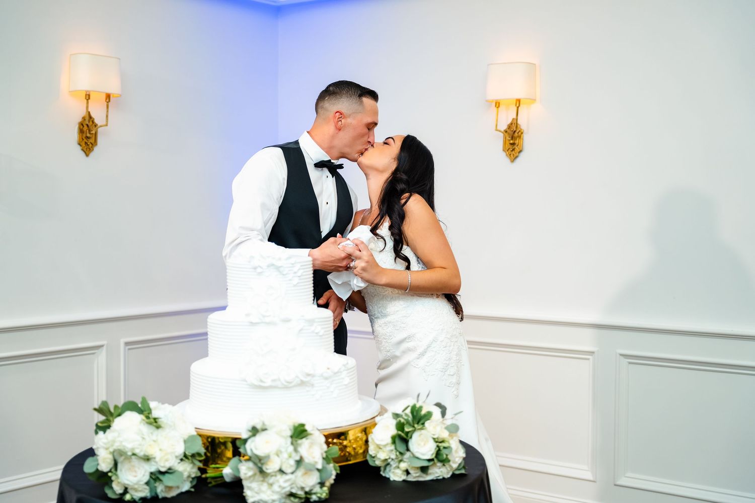 Elegant wedding cake cutting scene with white floral decorations and wall sconces.