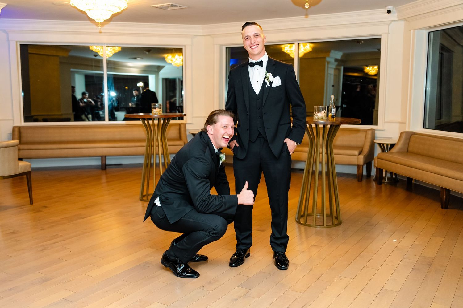 Groomsmen in black tuxedos pose together in an elegant ballroom setting.
