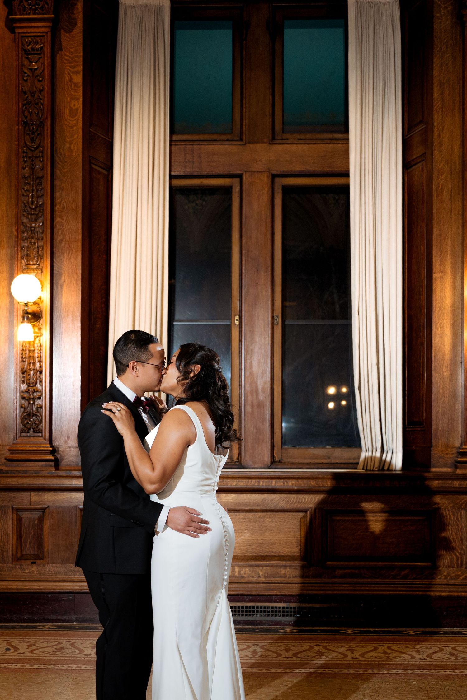 A couple shares an intimate dance moment in an elegant ballroom with ornate wood paneling and warm lighting.