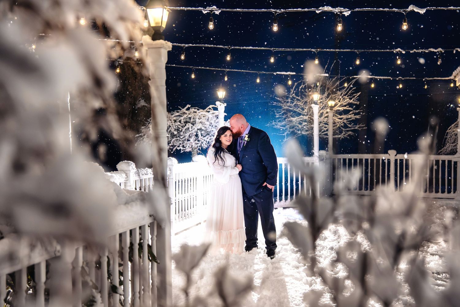 A snowy winter night scene with twinkling lights and white picket fences creating a magical holiday atmosphere.