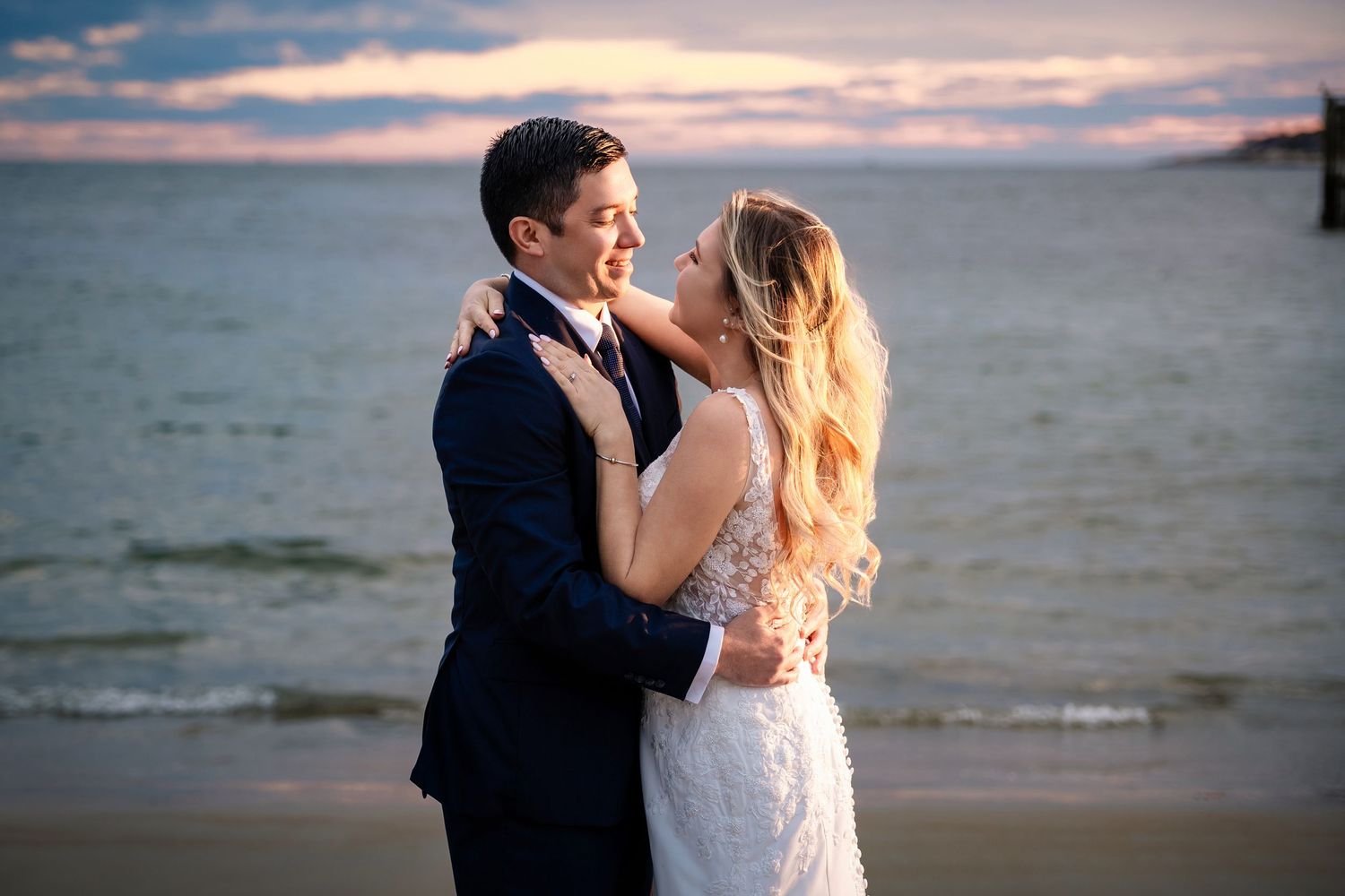 Couple embracing on beach at sunset with dramatic pink and purple sky.