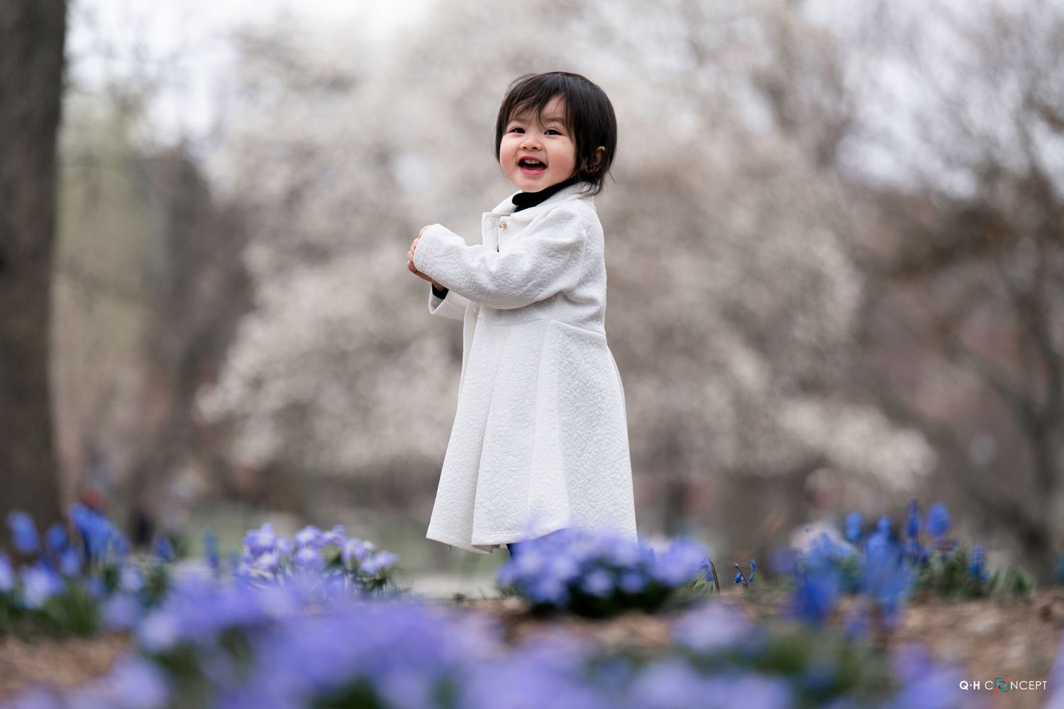 A child plays joyfully among blooming purple flowers in a spring garden setting.