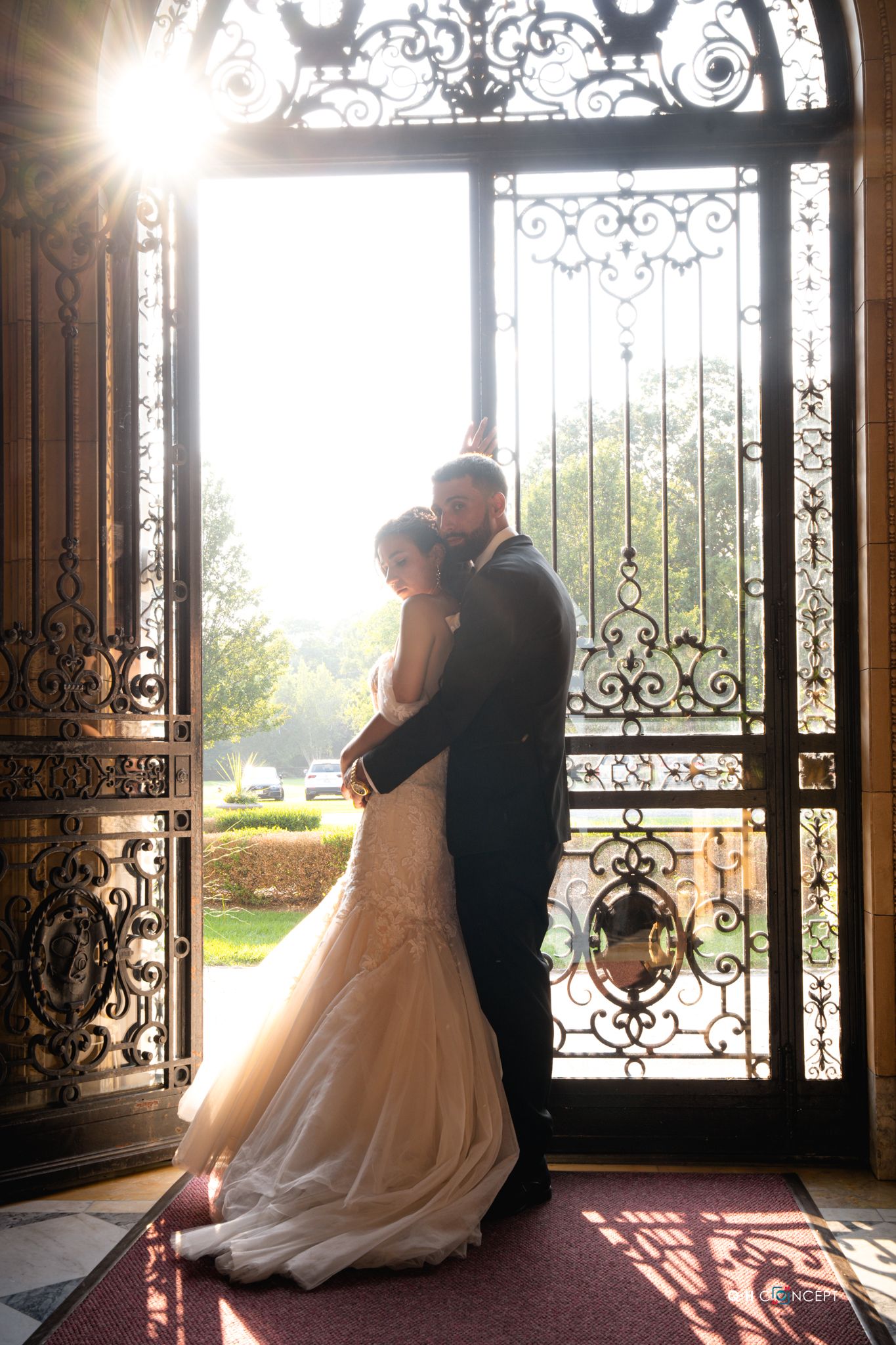Silhouetted couple shares romantic moments against ornate wrought iron doors in elegant wedding venue.