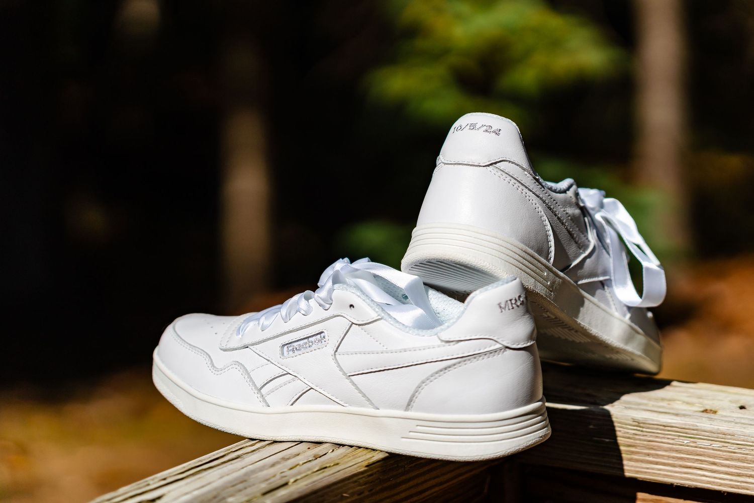 Close-up of white leather wedding shoes arranged on a wooden surface in natural light.