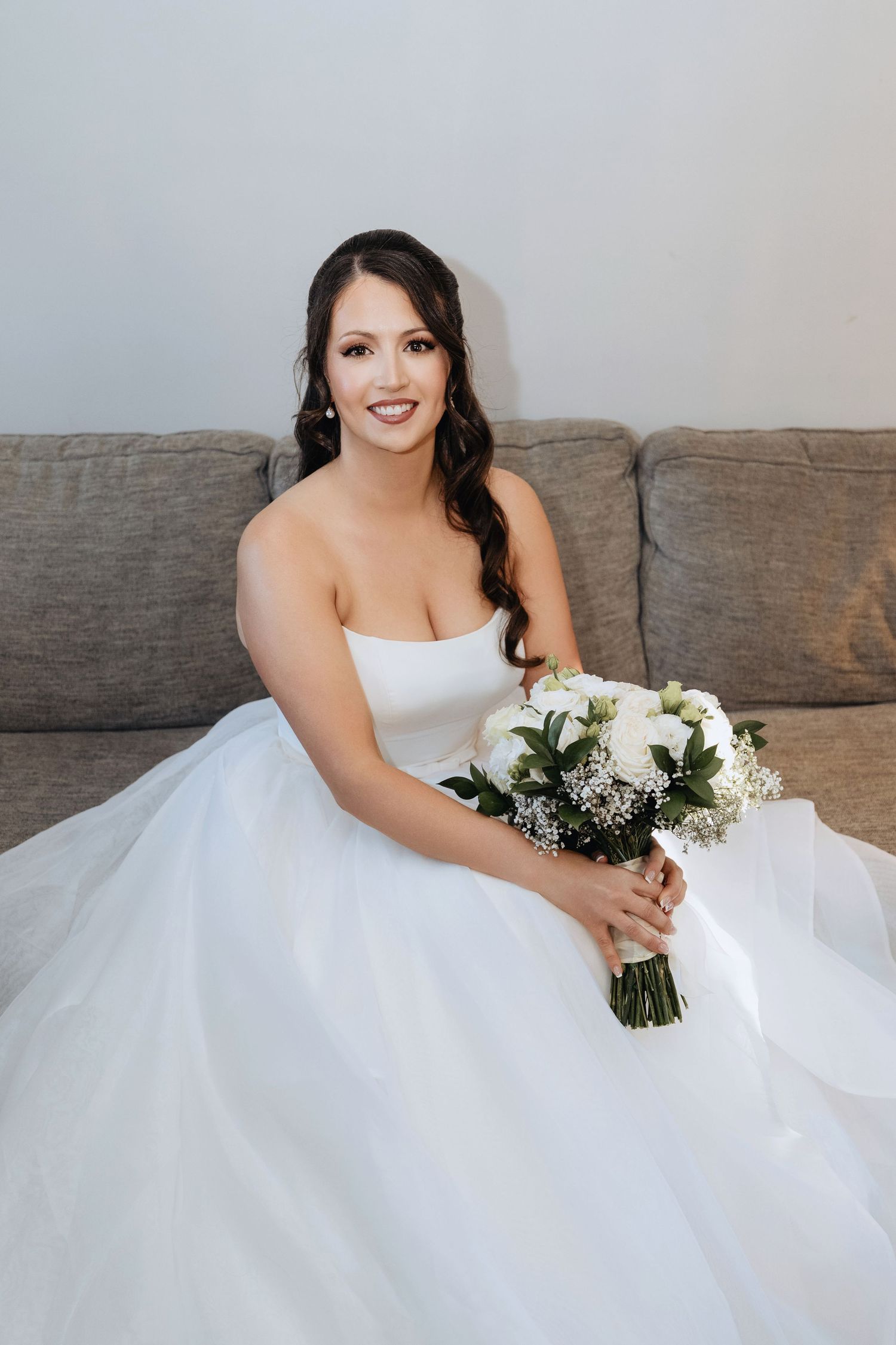 Elegant bridal portrait featuring white ballgown and bouquet against neutral background.