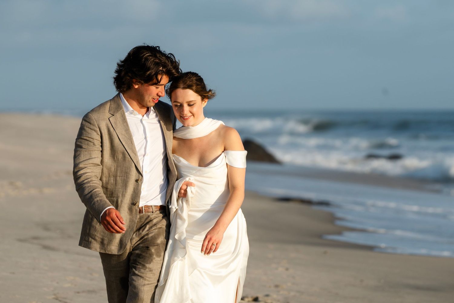 A romantic beach wedding photoshoot with waves crashing in the background at sunset.