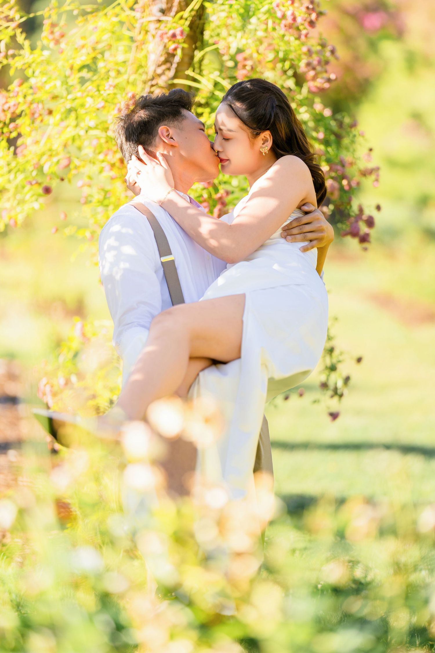 Couple sharing a tender moment among blooming spring flowers in bright sunlight.