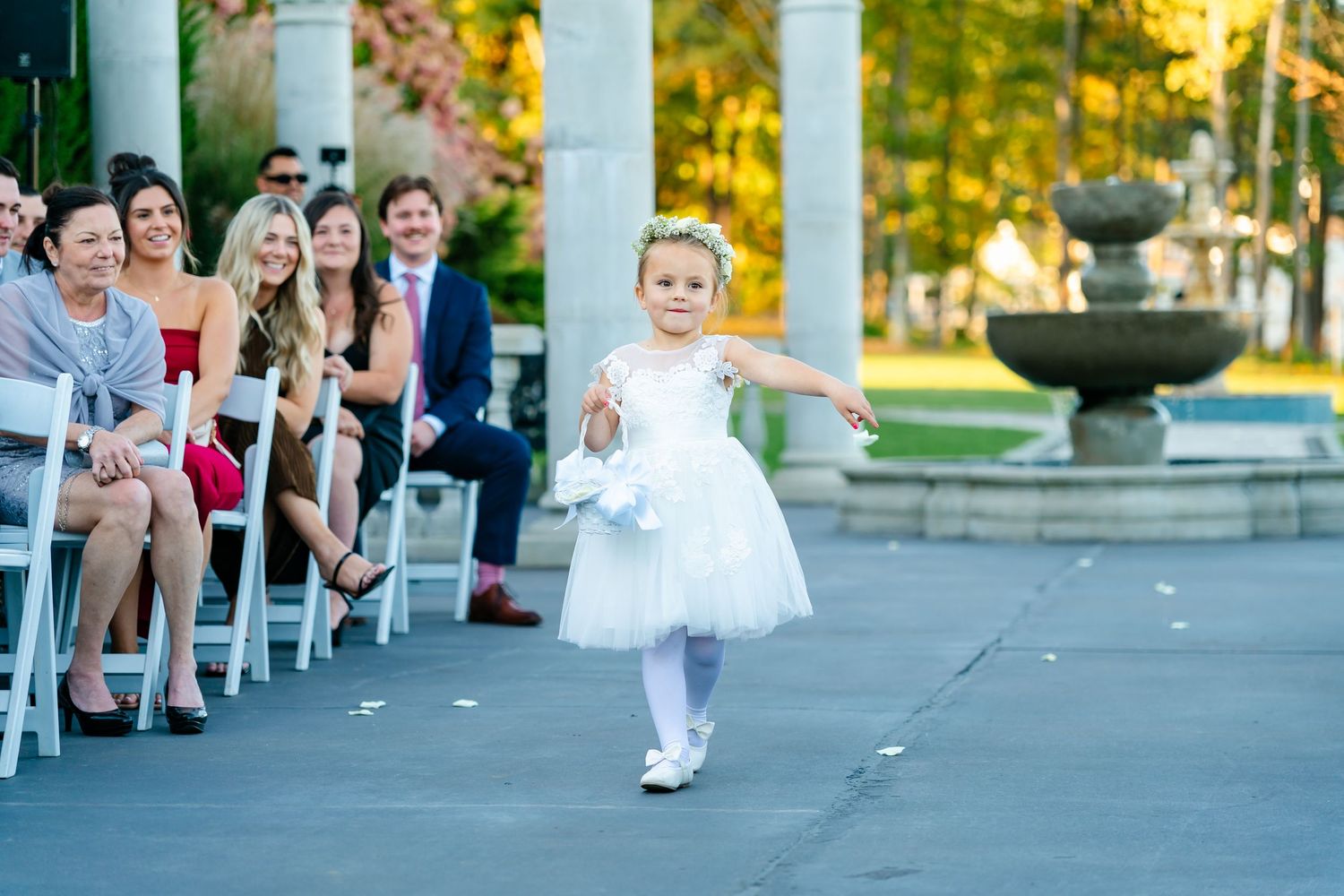 Wedding ceremony guests seated in white chairs along a columned outdoor walkway.