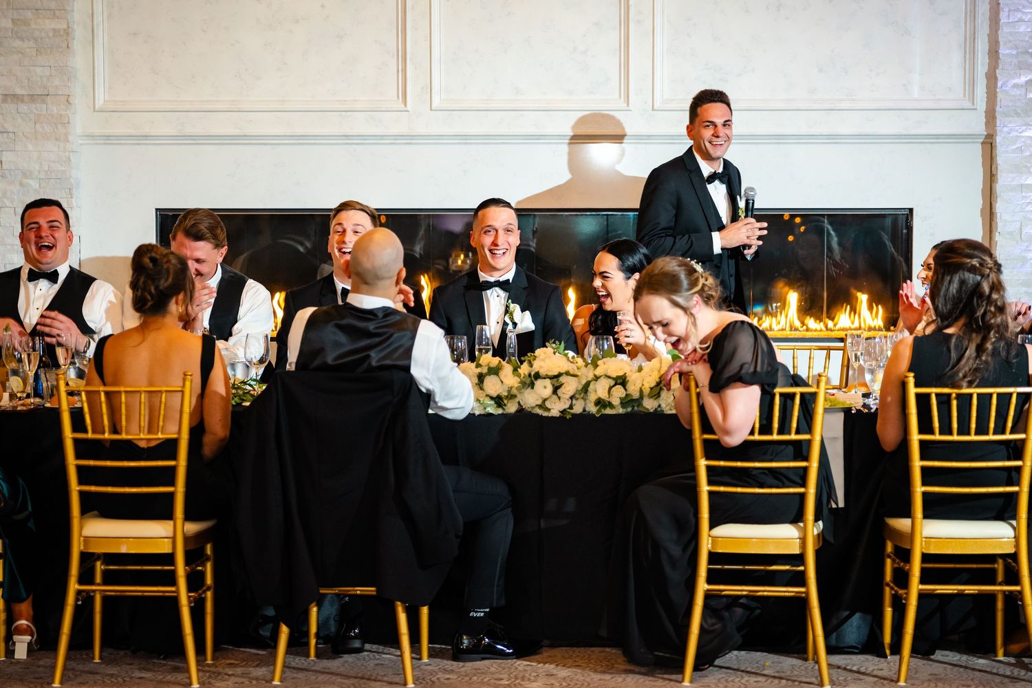 Elegant wedding reception setup with gold chairs and formal table settings in ballroom.