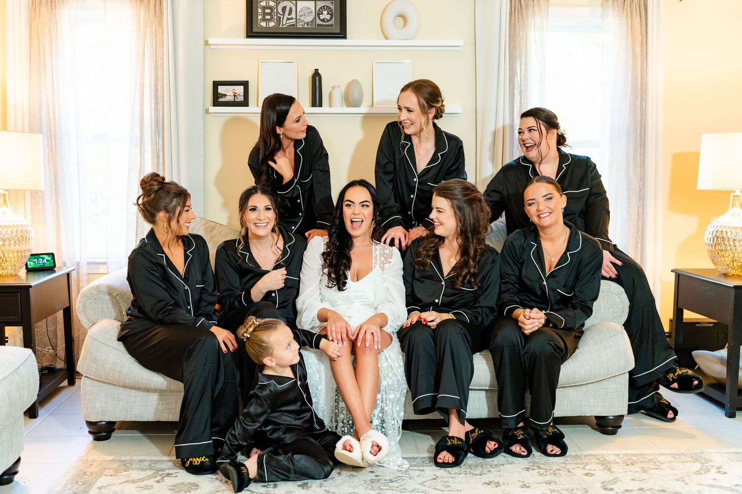 Wedding party members in black robes and white dresses relax together on a couch.