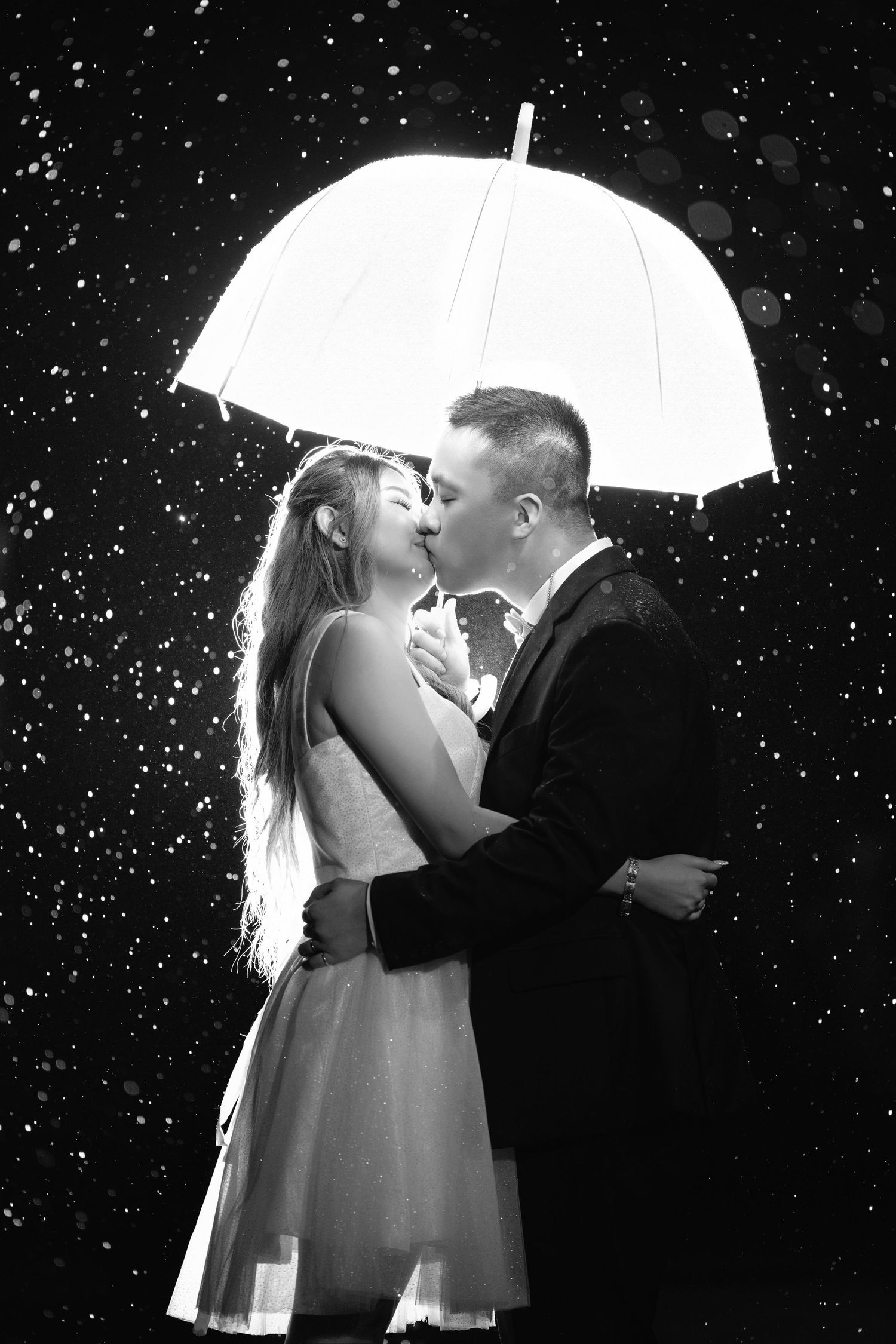 Romantic couple shares an intimate moment under a white umbrella in the falling snow.