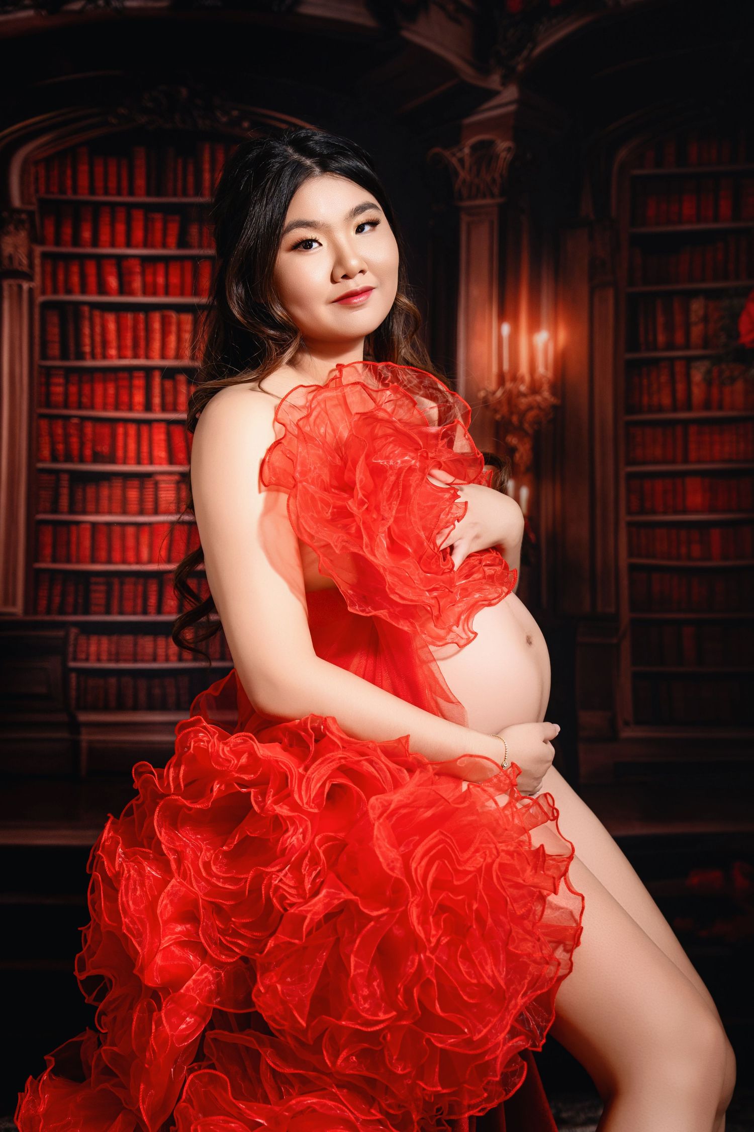 Boudoir maternity session in library with red ruffled dress and moody lighting.