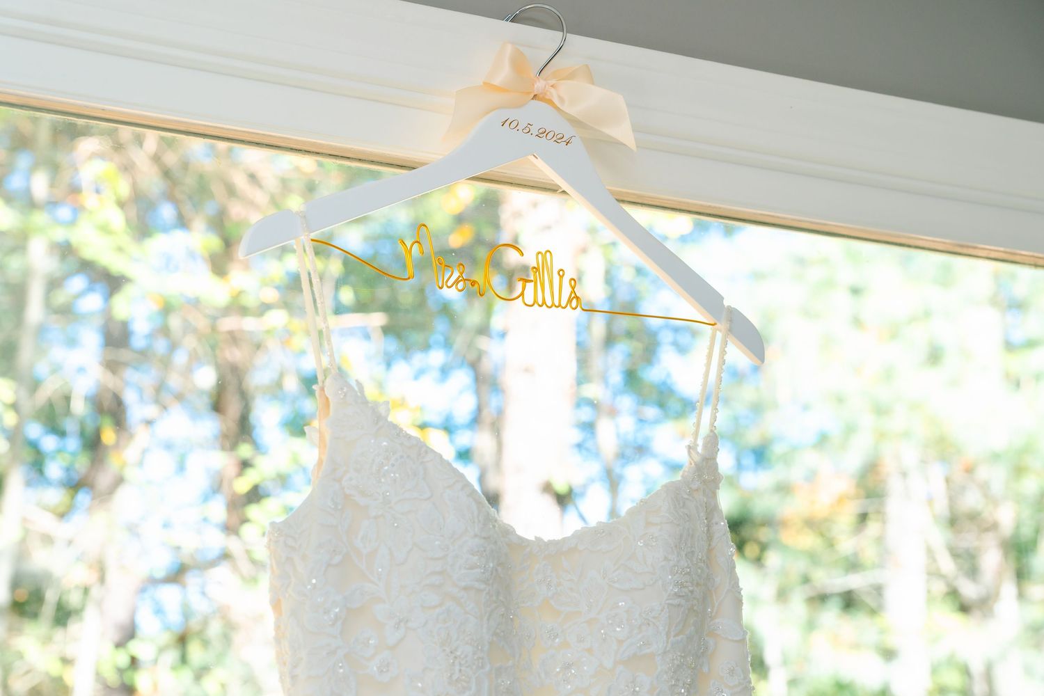 White wedding dress hangs by window with natural light streaming through.